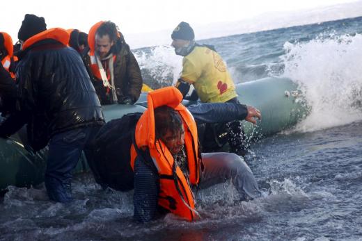 A refugee tries to stand up after falling into the sea as Syrian and Iraqi refugees arrive on a raft on a beach on the Greek island of Lesbos