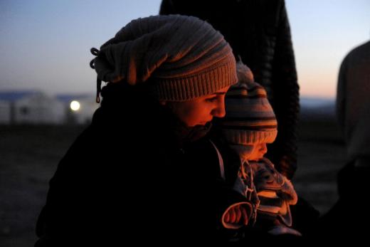 A Syrian refugee holds her baby next to a bonfire as she waits to cross the Greek-Macedonian border, near the village of Idomeni
